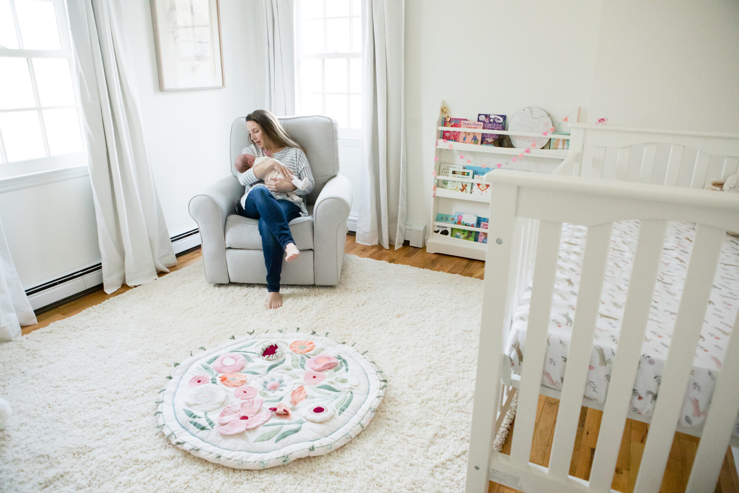 a young woman holds a baby in a bright white nursery Nanuet newborn photographer Milestone Images