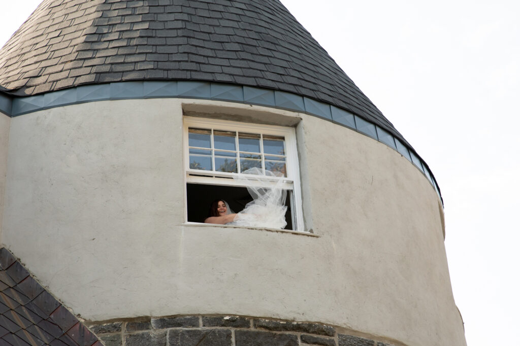 A bride's veil flows out of a tower as she leans out at the Mamaroneck Beach Club Westchester Wedding Photographer
