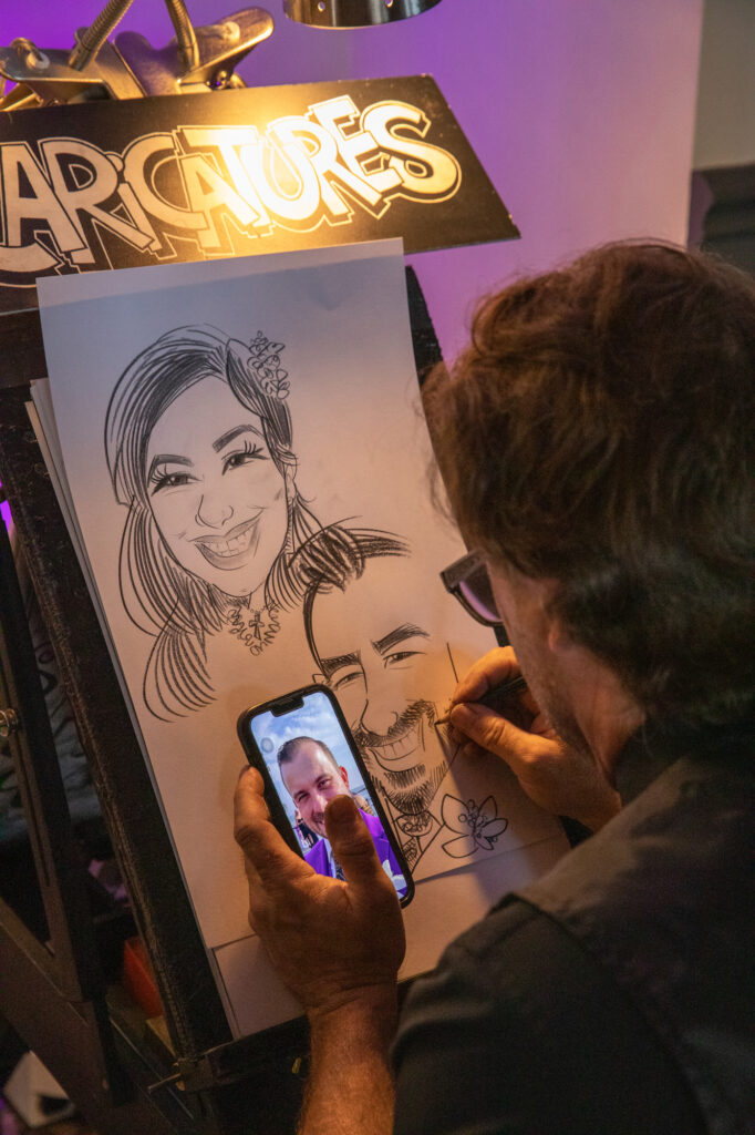 A caricature artist hired by Magical Memories Entertainment sketches the bride and groom during cocktail hour Westchester wedding Photographer Milestone Images