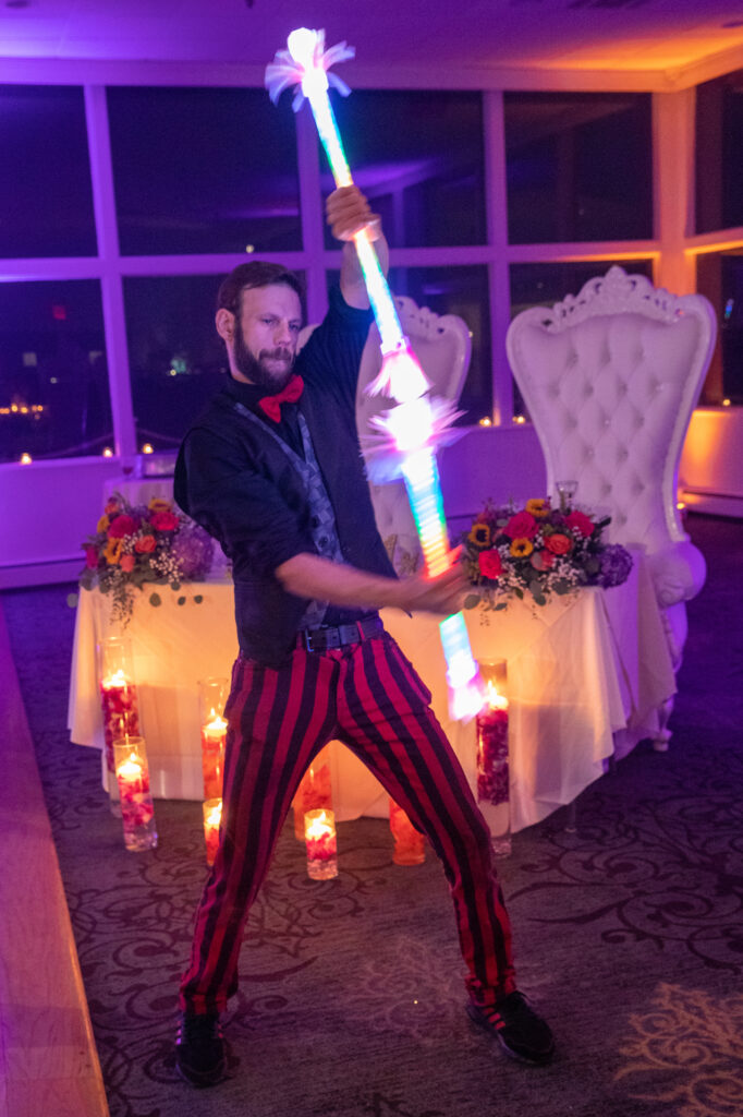 A male juggler in red and black striped pants twirls LED sticks at the reception Westchester wedding Photographer Milestone Images