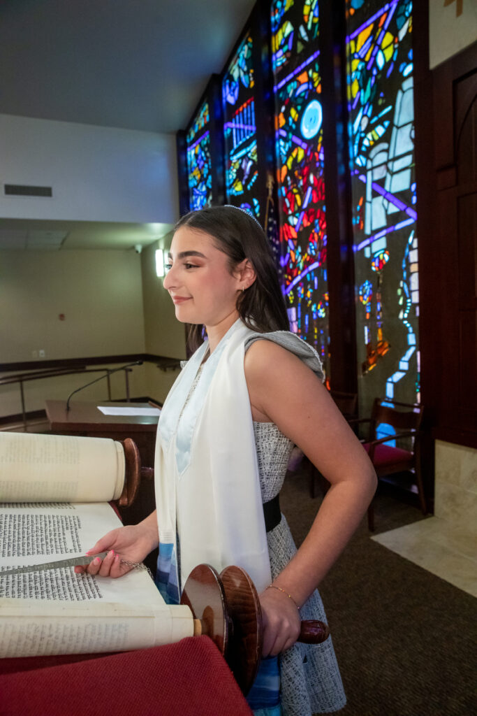 A teenage girl with long brown har points to a Torah scroll at Orangetown Jewish Center Rockland County Bat Mitzvah Photographer