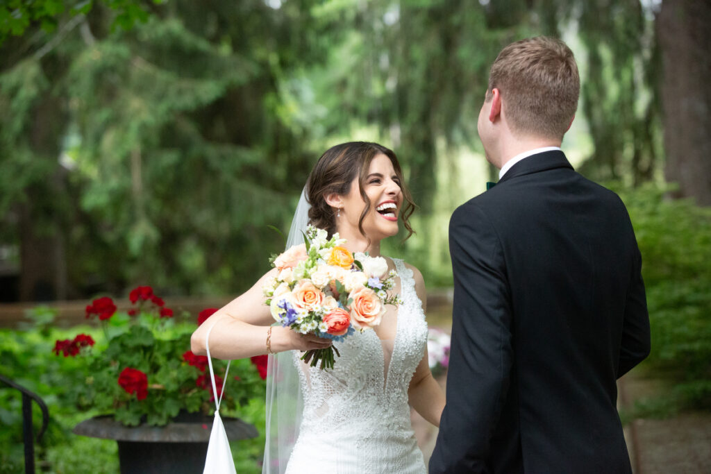 A bride grins at her groom during their first look in a garden Rockland County wedding photographer Milestone Images